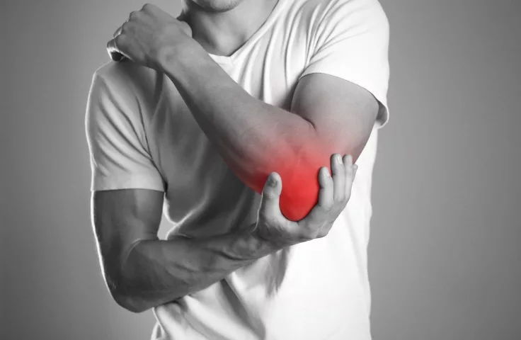 A man in a white T-shirt holding his painful elbow, with the sore area highlighted in red
