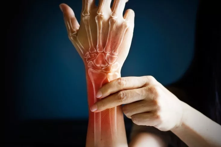 A person holding their sore wrist, with the bones of the hand and wrist shown in a red overlay