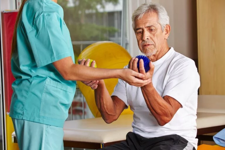 An occupational therapist helping an older man grip a therapy ball