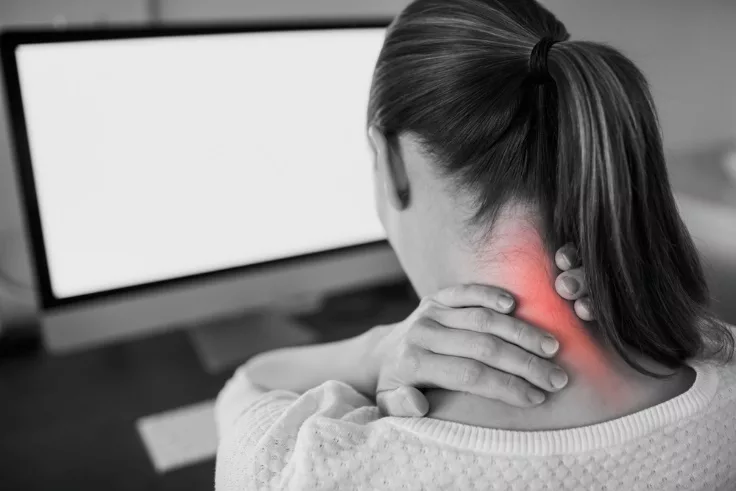 A woman at her computer rubbing the back of her sore neck