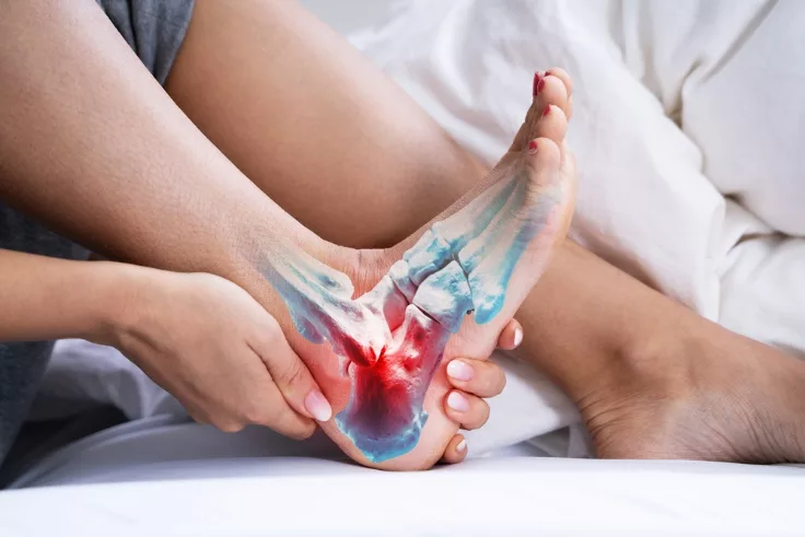 A person sitting on a bed holding a sore foot, with the bones of the foot and ankle highlighted