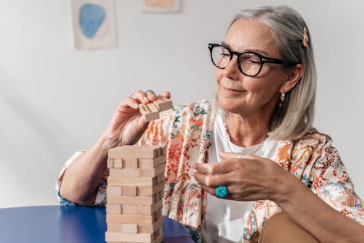 A senior woman wearing glasses carefully removes a block from a Jenga tower, representing balance and fall prevention at Health and Fitness Professionals physical therapy Woodbridge NJ.